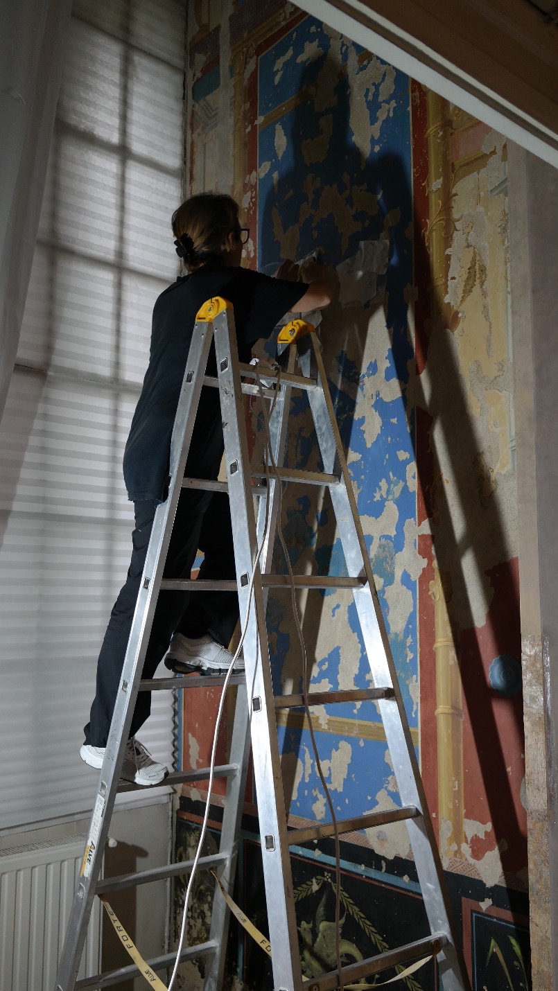 Elena Martin pe o scară, lucrând la o pictură murală de perete